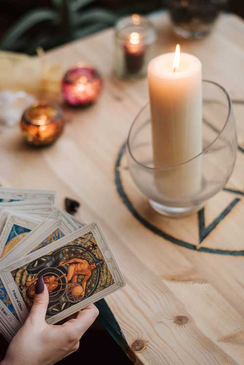 Visione dall'alto delle mani di una cartomante con set di carte dei tarocchi vicino a candele accese durante un consulto di lettura dei tarocchi